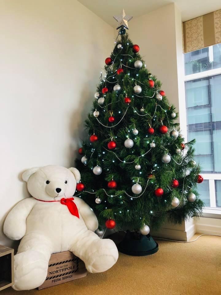 A Christmas tree decorated with red and silver baubles beside a teddy bear